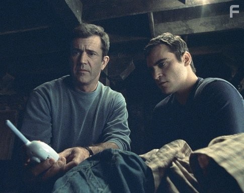 A baby monitor provides a message from above for Graham (Mel Gibson, left) and his brother, Merrill (Joaquin Phoenix, right).
